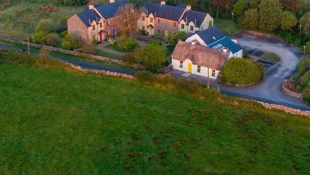 A rural landscape with a cluster of stone houses, a winding road, and a dense forest in the background. - Burren Court Lodge (Ballyvaughan)