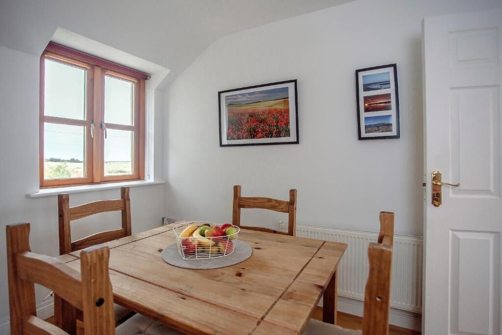 A dining area with a wooden table, chairs, a fruit basket, and framed pictures on the wall.
