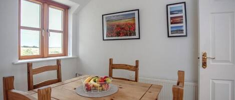 Een eethoek met een houten tafel, stoelen, een fruitmand en ingekaderde foto's aan de muur.