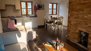 A cozy living room with a fireplace, a dining area with a table and chairs, a kitchen with cabinets and a microwave, and a sofa with a throw pillow. - Burren Court Lodge (Ballyvaughan)
