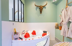 A bathroom with a round bathtub, a bull skull decoration, a bottle of champagne, and a robe rack.