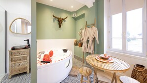 Ein Badezimmer mit einem großen Spiegel, einem an der Wand befestigten Stierkopf, einer Badewanne, einem runden Tisch mit einer Obstschale und einem Fenster mit Aussicht.