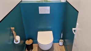 Une petite salle de bain comprenant des toilettes, un bidet, un porte-rouleau de papier toilette et un sèche-mains.
