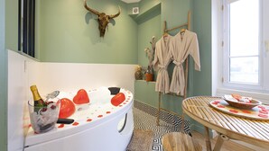 Ein Badezimmer mit Badewanne, einem Stierkopf als Dekoration, einer Champagnerflasche und einem Handtuchhalter mit Bademänteln.