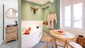 Une salle de bain avec une grande baignoire, un miroir, un meuble en bois, une table ronde en bois et une fenêtre.