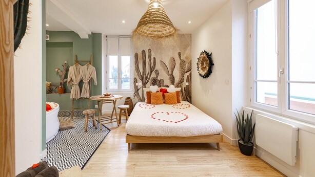 Ein modernes Schlafzimmer mit einem Bett, einer Deckenleuchte, einer Wand mit Kakteengemälde und einem Fenster.