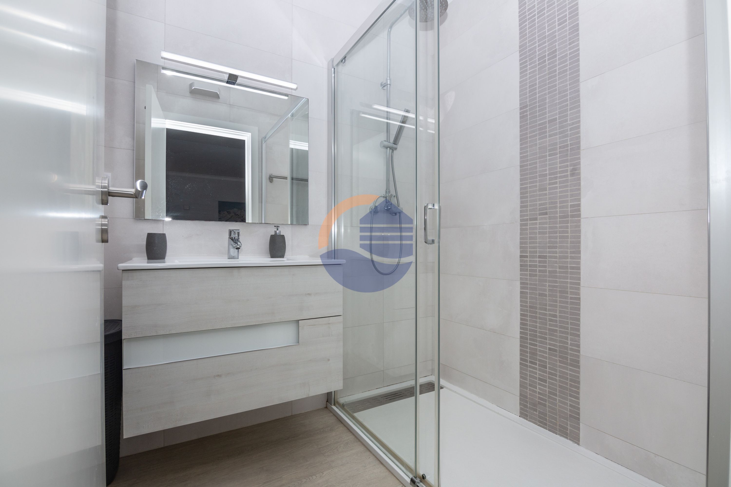 Un baño moderno con cabina de ducha de vidrio, tocador blanco con espejo y pared de ducha con azulejos.