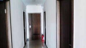 A narrow hallway with a wooden door at the end, a fire extinguisher on the wall, and a white ceiling. - Chashan Hostel (Shanghai)