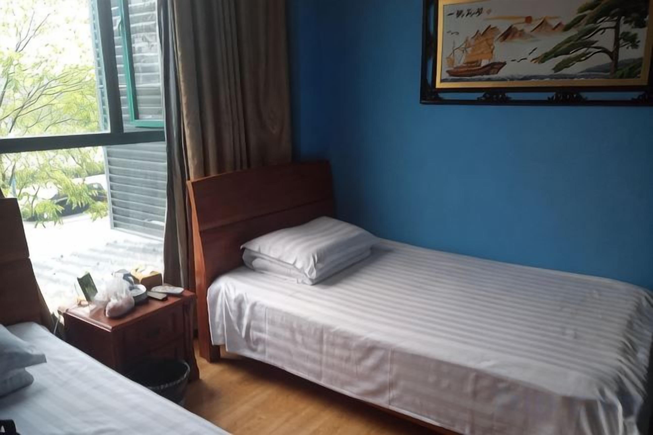 A single bed with a wooden headboard, a bedside table with a lamp, and a window with curtains.
