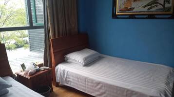 A single bed with a wooden headboard, a bedside table with a lamp, and a window with curtains.