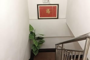 A staircase with a metal railing, a framed picture on the wall, and a green plant. - Chashan Hostel (Shanghai)