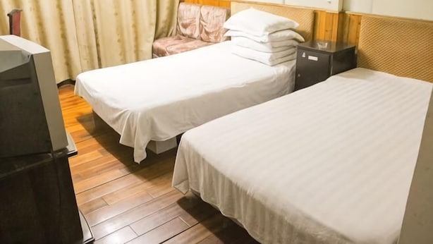 A hotel room with two single beds, a wooden floor, a television, and a chair. - Chashan Hostel (Shanghai)