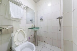 Un baño con inodoro, lavabo de cristal, ducha y espejo.