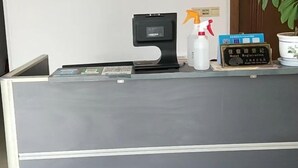 A reception desk with a black counter, a white spray bottle, a black device, and a sign with hotel registration instructions. - Chashan Hostel (Shanghai)