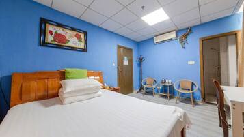 A hotel room with a bed, a chair, a table, and a door.