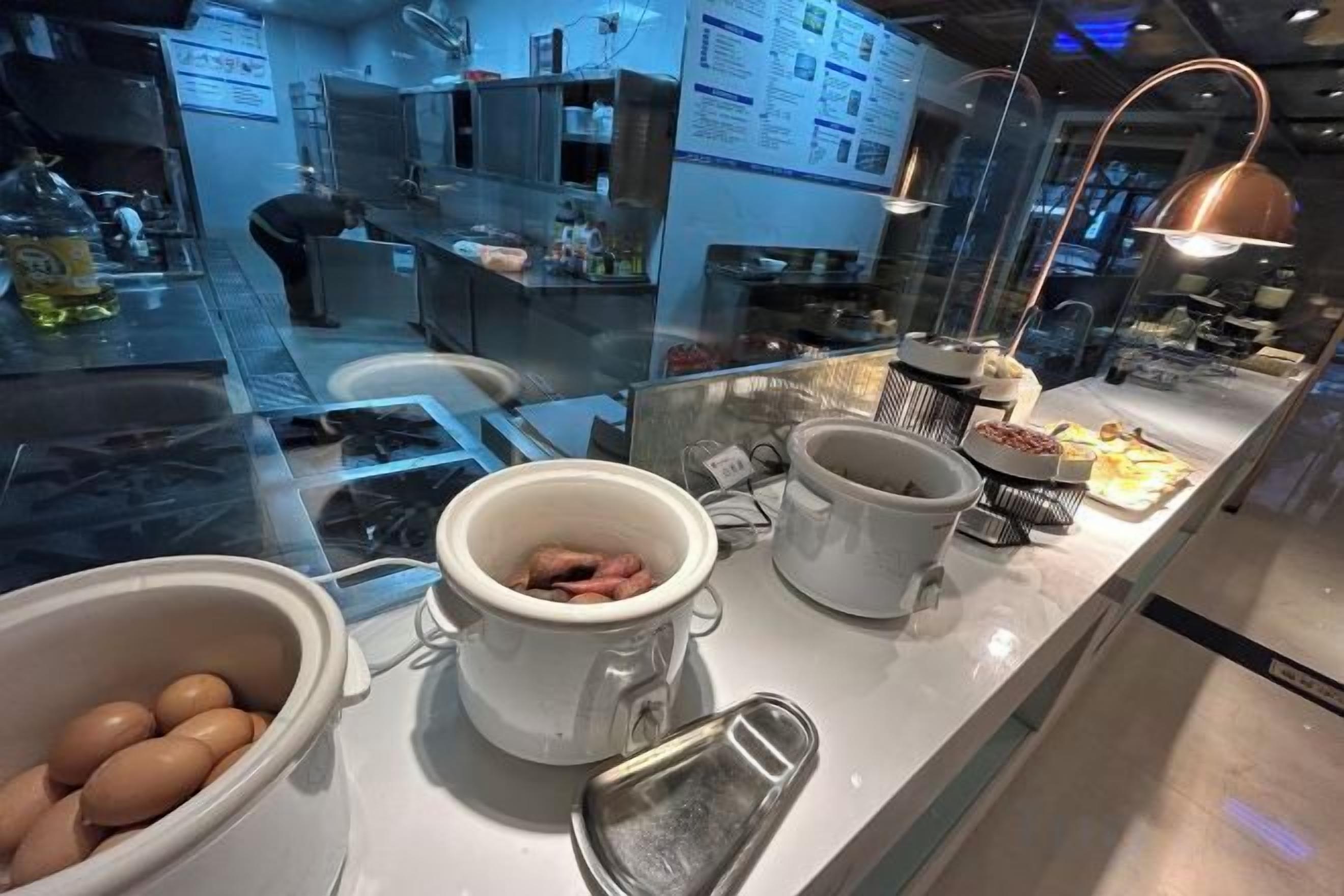 Uma área de cozinha com divisória de vidro, diversos utensílios de cozinha e alimentos sobre o balcão.