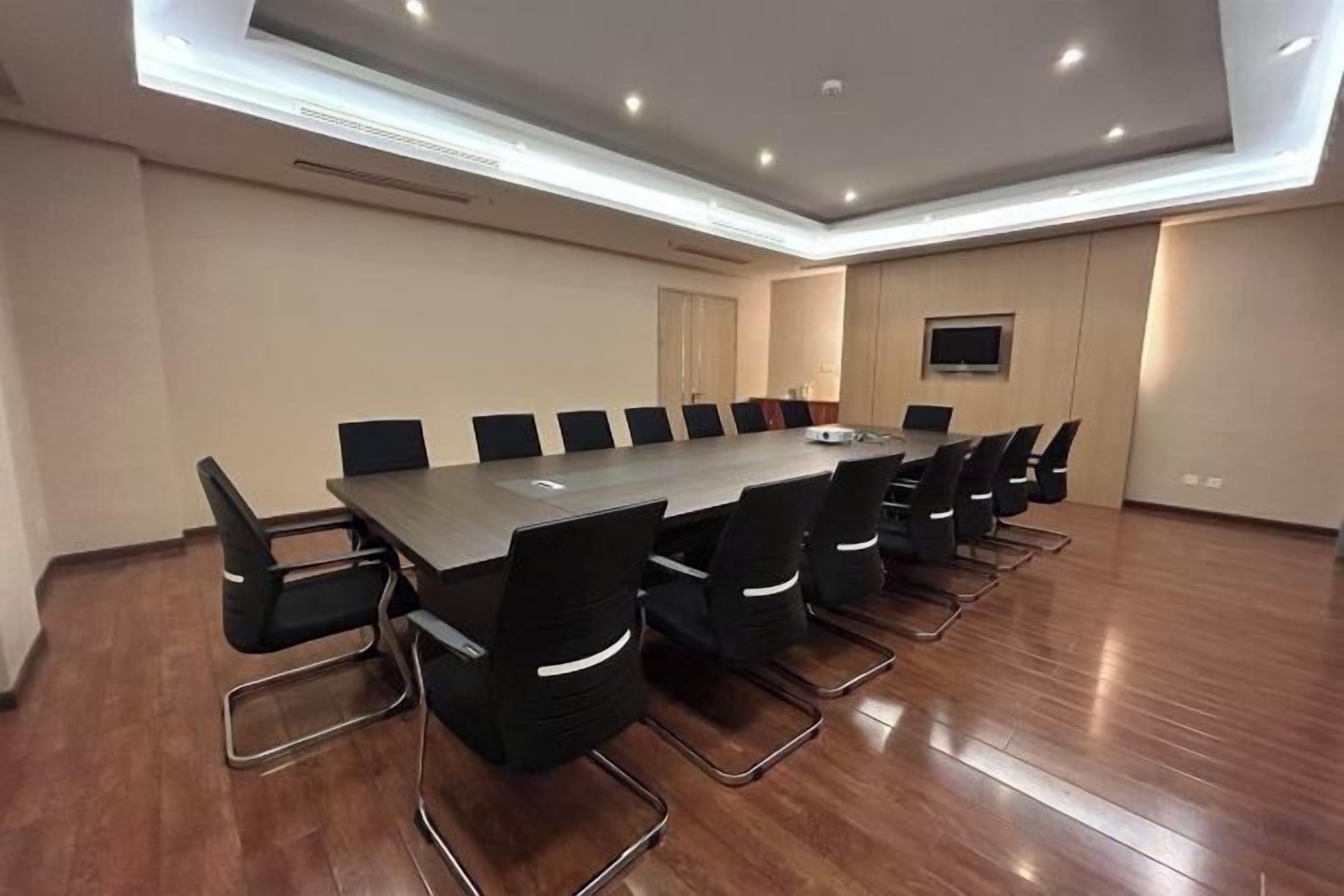 A conference room with a long table and chairs, a flat-screen TV, and a ceiling light fixture.
