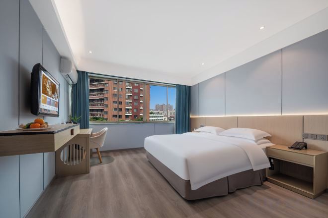 A modern hotel room with a bed, desk, chair, and a city view.