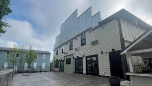 A modern building with a flat roof and large windows, a concrete patio area with steps leading to the entrance, and a small outdoor seating area with tables and chairs. - The Grant Hotel and Venue (Buchanan)