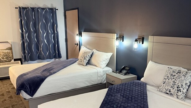 A hotel room with two beds, a bedside table with a phone, and a wall-mounted light fixture. - The Grant Hotel and Venue (Buchanan)