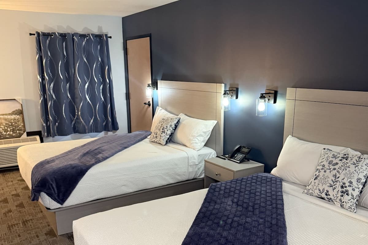 A hotel room with two beds, a bedside table with a phone, and a wall-mounted light fixture.