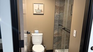 A compact bathroom with a toilet, a shower, and a glass-enclosed shower stall. - The Grant Hotel and Venue (Buchanan)