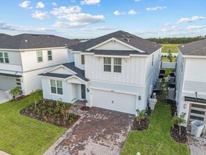 A modern residential building with a garage, a small front yard with plants, and a paved driveway. - Super Homey (Clermont)
