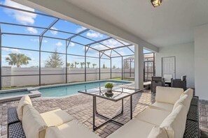A poolside area with a glass table, white cushioned seating, and a view of the pool and palm trees. - Super Homey (Clermont)