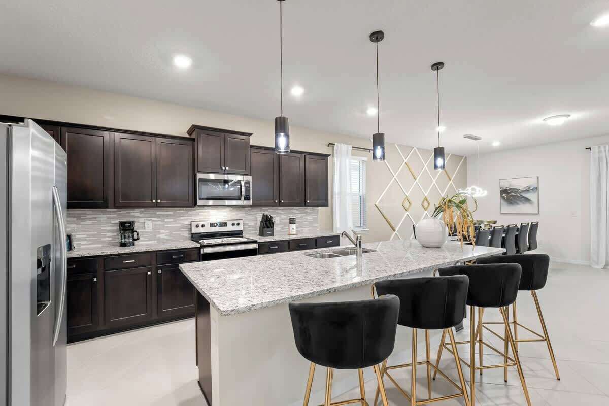 A modern kitchen with dark cabinets, a granite countertop, stainless steel appliances, pendant lighting, and a bar area with stools.