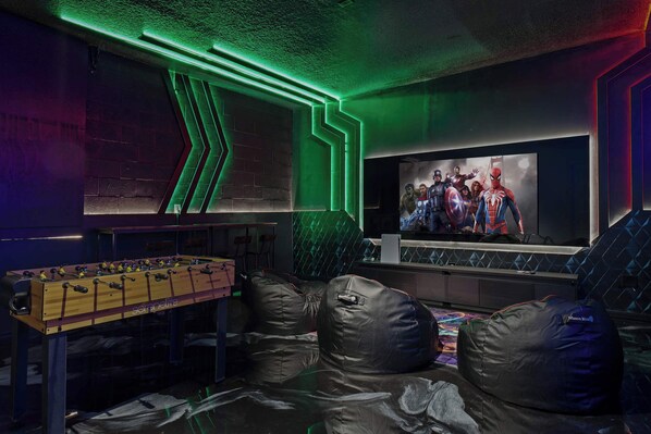 A room with a foosball table, bean bags, and a large TV screen displaying a movie scene. - Super Homey (Clermont)