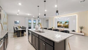 A modern kitchen with a central island, pendant lighting, and a dining area with a view. - Super Homey (Clermont)
