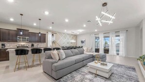 A modern living room with a grey sectional sofa, a white coffee table, and black bar stools. - Super Homey (Clermont)