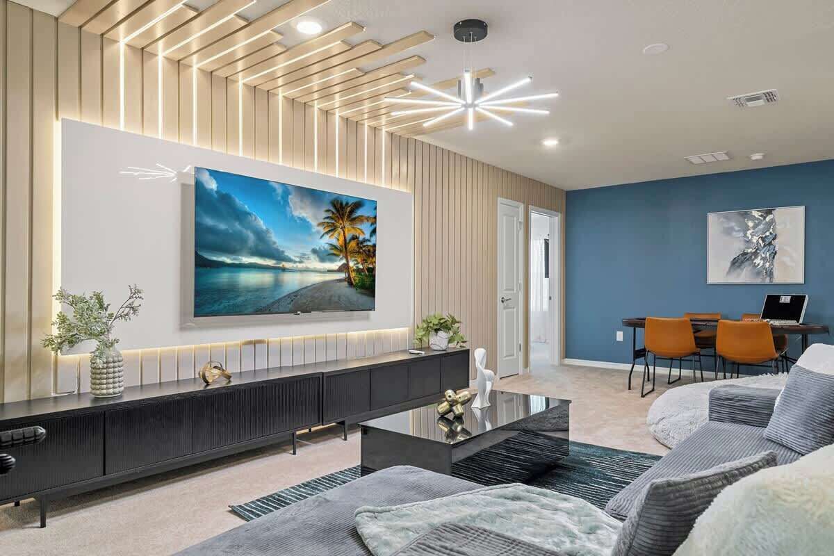 A modern living room with a large TV, a sofa, a coffee table, and a dining area with chairs.