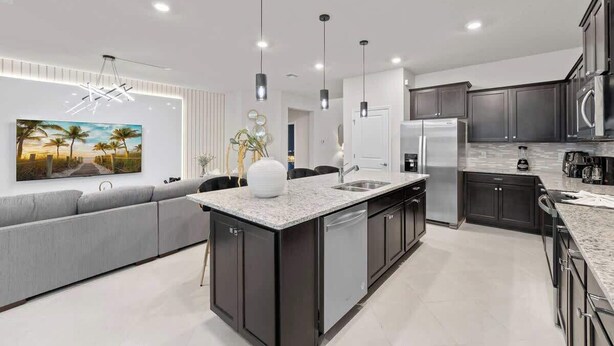 A modern kitchen with dark cabinetry, a central island, and pendant lighting. - Super Homey (Clermont)