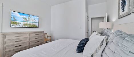 Un dormitorio con una cama, un aparador, un televisor en la pared y una puerta que da a otra habitación.