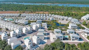 A resort with multiple white buildings, a central pool, and a view of a lake and forest.