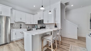 A modern kitchen with white cabinetry, stainless steel appliances, and a central island with bar stools.