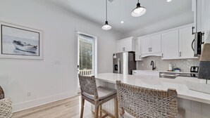 A modern kitchen with white cabinetry, a stainless steel refrigerator, and a bar area with macrame chairs.