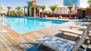 A swimming pool with wooden deck and lounge chairs, surrounded by palm trees and a brick wall.