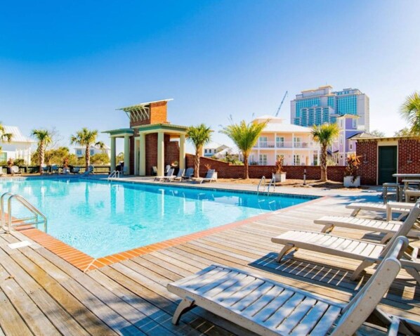 A swimming pool with wooden deck and lounge chairs, surrounded by palm trees and a brick wall.