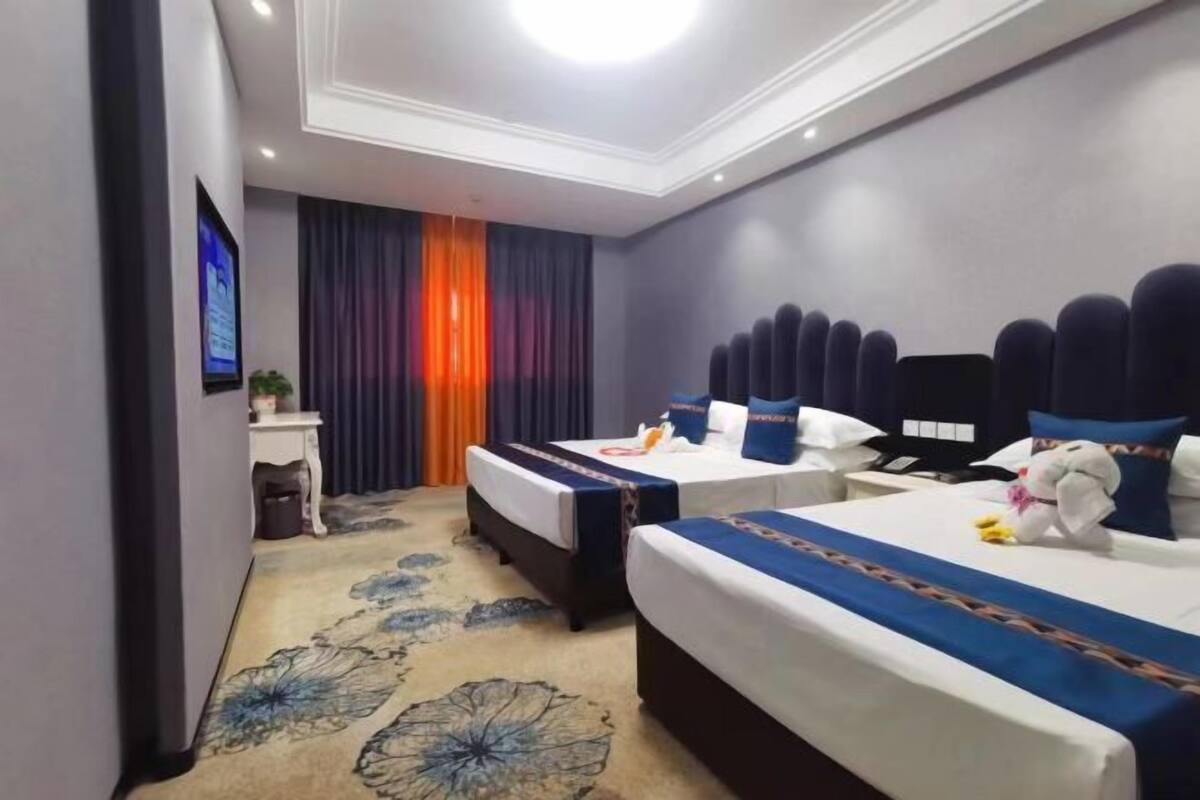 A hotel room with two beds, a desk, a TV, and a decorative curtain.