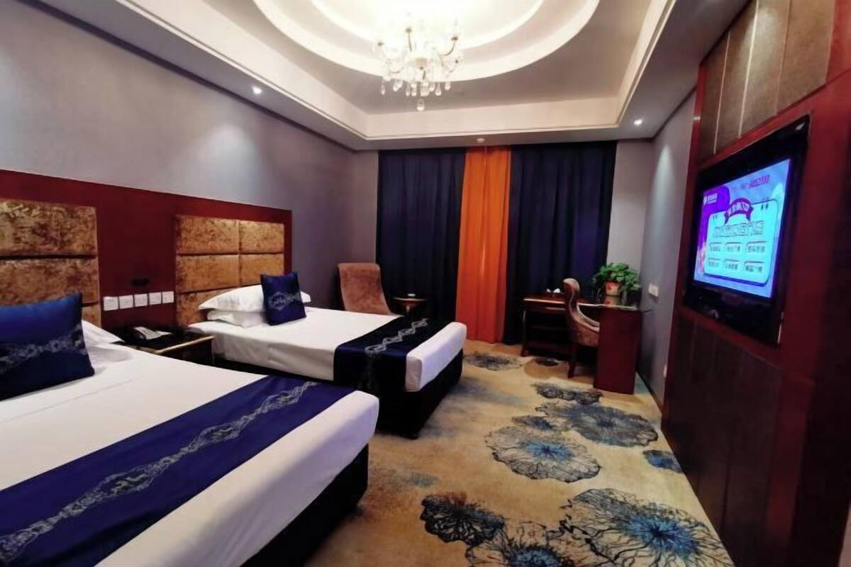 A hotel room with two beds, a TV, a desk, and a chandelier.