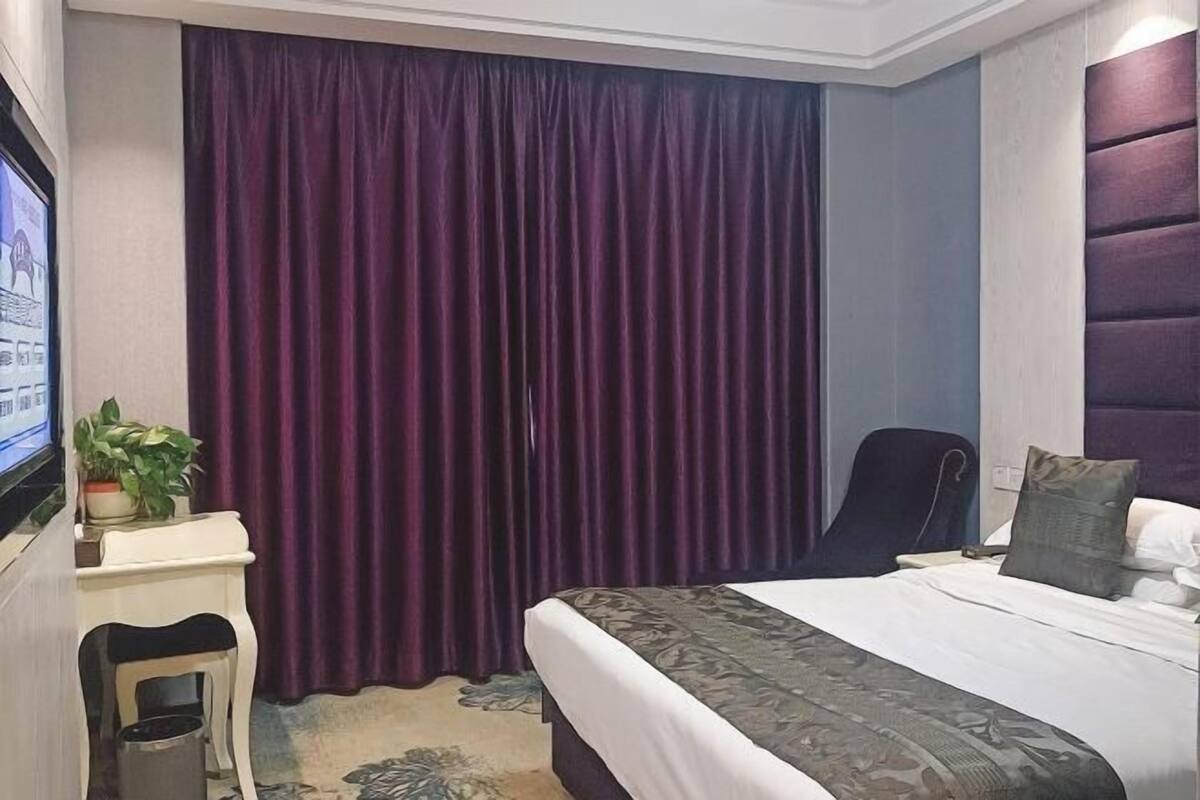 A hotel room with a bed, a desk with a plant, a chair, and a TV.