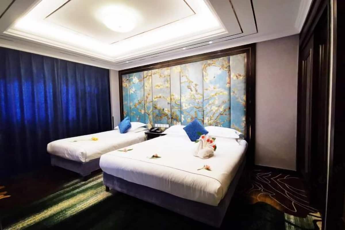 A hotel room with two beds, a large window with a floral pattern, and a dark blue curtain.