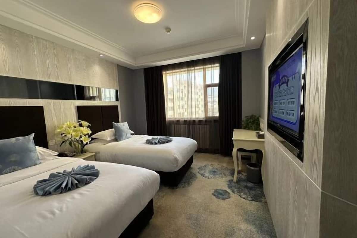 A hotel room with two beds, a TV, a desk, and a window with curtains.