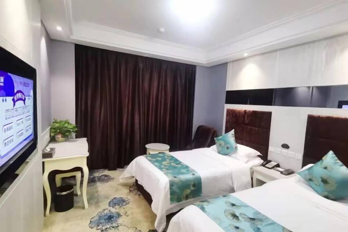 A hotel room with two beds, a TV, a desk, a chair, and a curtain.