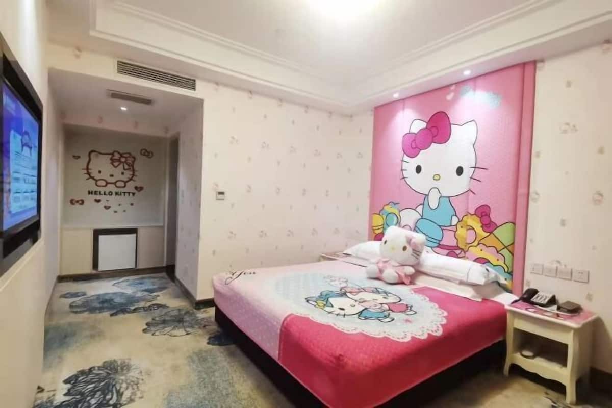 A room with a bed featuring Hello Kitty decorations, a small bedside table with a phone, and a wall with Hello Kitty artwork.