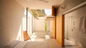 Un baño moderno con ducha, una cama y un ventanal grande.