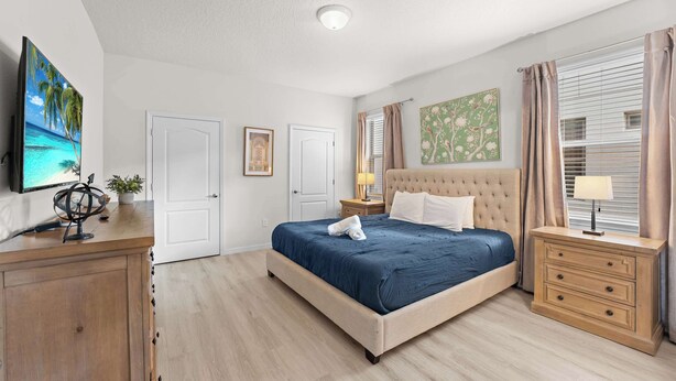 A bedroom with a bed, bedside tables, a dresser, a television, and artwork on the walls. - Super Play (Kissimmee)