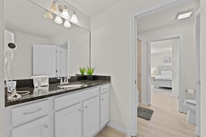 A modern bathroom with a large mirror, white cabinets, a black countertop, and a hairdryer. - Super Play (Kissimmee)